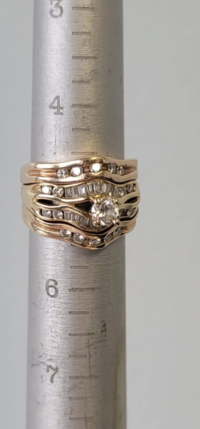 A diamond and gold ring set measured on a metal ring sizer during an appraisal