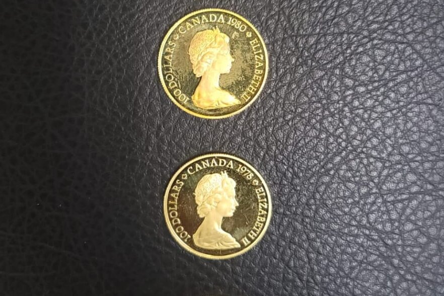 Two Canadian $100 gold coins from 1978 and 1980 on a dark leather surface